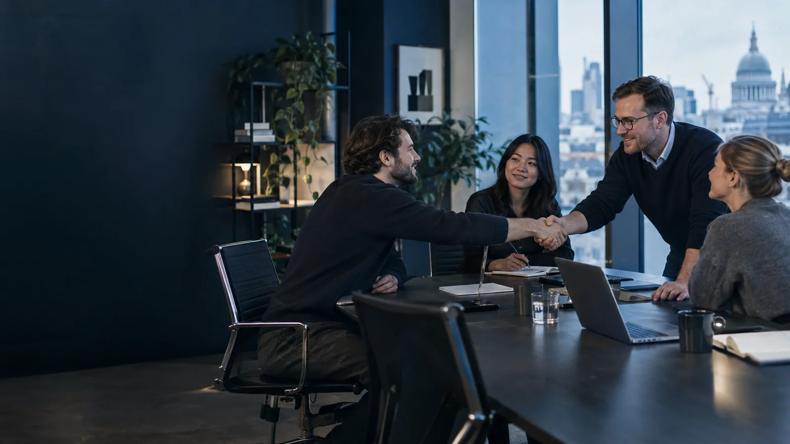 Startup team marking a funding milestone with a handshake during a meeting in a London office.